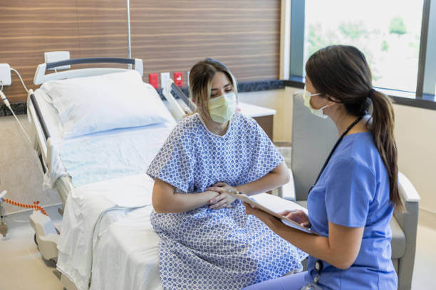 The female patient grabs her stomach in pain as she sits with the nurse to review symptoms.