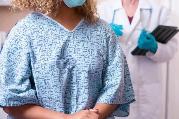 Young African American woman prepares for a breast exam, mammogram from her gynecologist doctor at hospital or clinic. Women's health issues. Breast Cancer awareness.