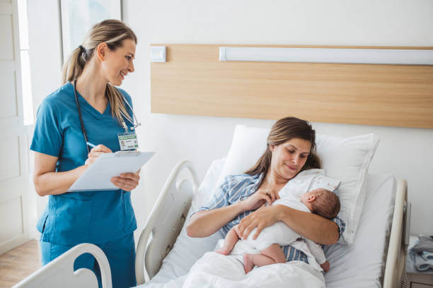 Nurse taking personal data from mother and talking to her. Mother holding newborn baby.