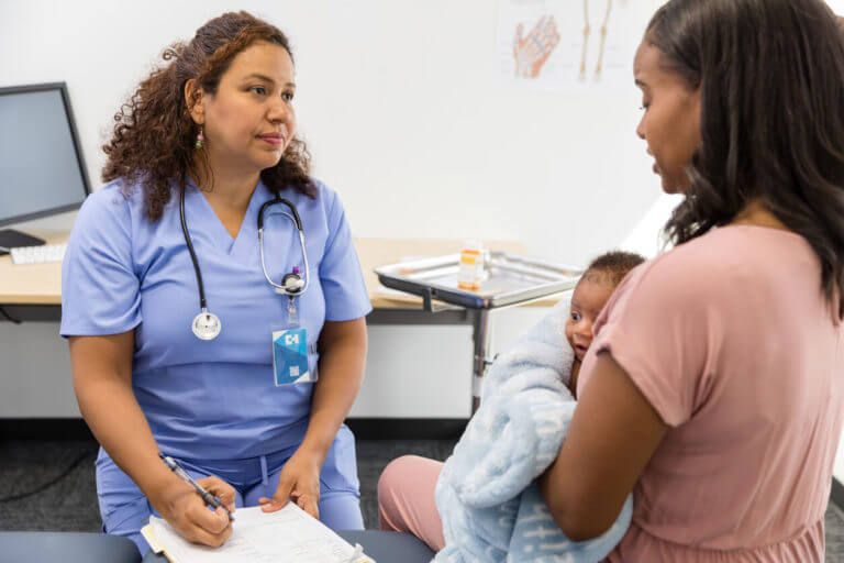 mother holding her newborn baby talking to obgyn about postpartum care