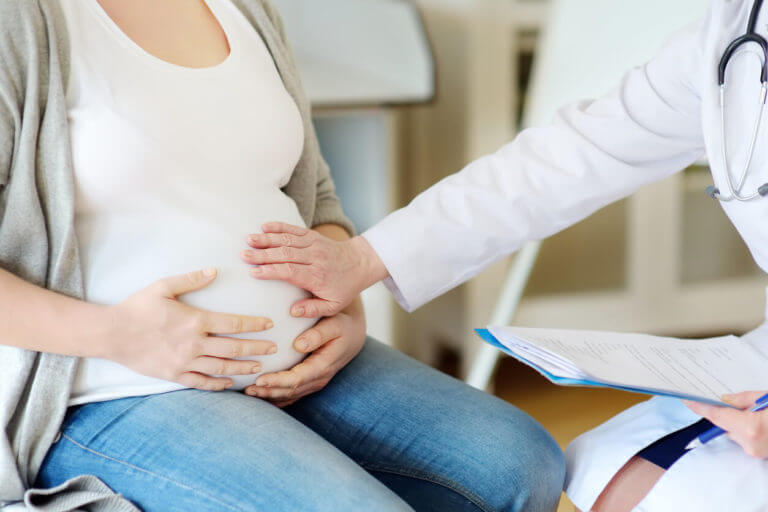 OBGYN feeling pregnant woman's belly and giving guidance on family planning during counseling appointment.